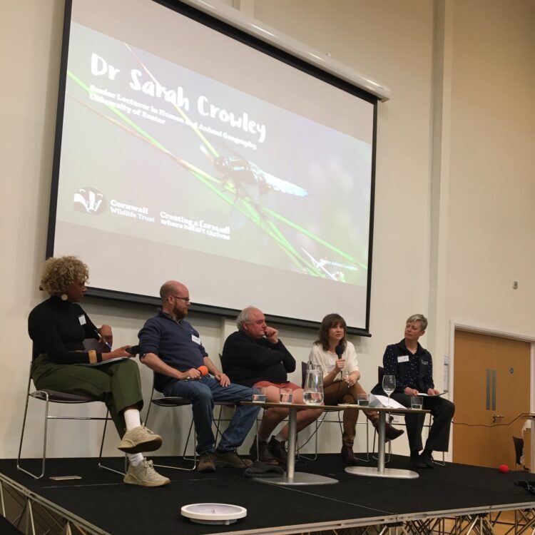 Sarah Crowley sits on a stage with a panel of three other people and a projected image